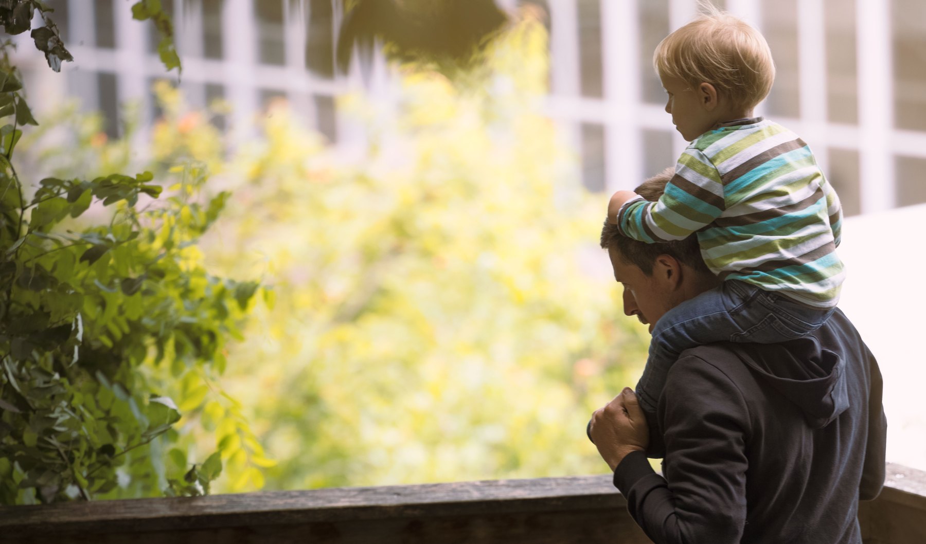 Ein Vater tr&auml;gt ein Kleinkind auf den Schultern auf einem Gartenbalkon